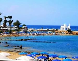 a beach with blue umbrellas and people in the water at Maria Holiday Apartments in Protaras