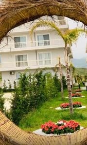 a large white building with a palm tree and flowers at R&I Sea and Mountain View Apartments Radhimë in Orikum