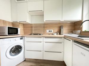 a kitchen with white cabinets and a washer and dryer at Pastelowe Studio - Comfy Apartments in Gdańsk