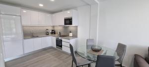 a white kitchen with a glass table and chairs at Villa Castanho I in Calheta