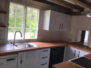 a kitchen with white cabinets and a sink and two windows at Thatched Cottage Wix in Wix