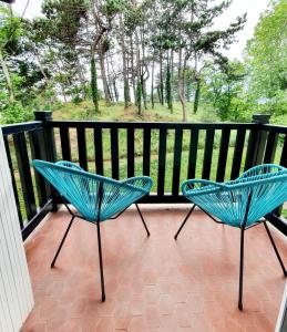 two blue chairs on a balcony with trees in the background at Le bord de plage in Bénerville-sur-Mer