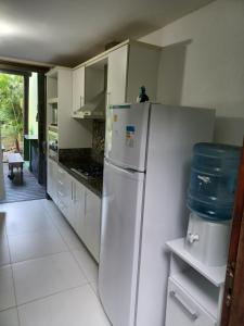 a white kitchen with a white refrigerator and cabinets at Bangalô duplex à beira-mar in Camaçari
