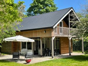 een hut met een terras met stoelen en een parasol bij Tofino, een comfortabel vakantiehuis naast een bos en zwemmeer in Gasselte