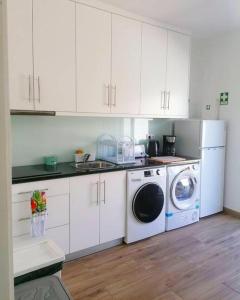 cocina con armarios blancos, lavadora y secadora en Pirata Milfontes Guest House, en Vila Nova de Milfontes