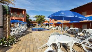 a patio with white chairs and blue umbrellas and a pool at Pousada Estalagem Da Serra in Serra do Cipo