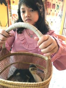 a young girl holding a basket with a duck in it at Baan Til Dao Pround Fah in Ban Na Sok