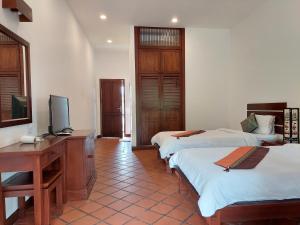 a room with two beds and a desk and a television at Villa Chitchareune 2 in Luang Prabang