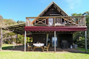 a house with a deck with a table and chairs at Alcheringa Cottage Amazing Location with views in Kangaroo Valley