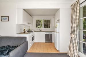 a kitchen with white cabinets and a couch in a room at Alcheringa Cottage Amazing Location with views in Kangaroo Valley