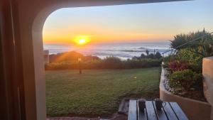 a view of a sunset from a window with a bench at Eden Dunes - Shelly Beach in Margate