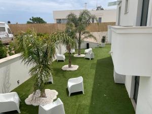 a balcony with white chairs and palm trees on the grass at Tuo Hotel in Polignano a Mare