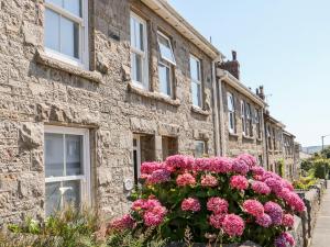 a stone house with pink flowers in front of it at Mazey Cottage in Penzance