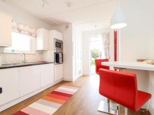 a white kitchen with red chairs and a table at Mazey Cottage in Penzance
