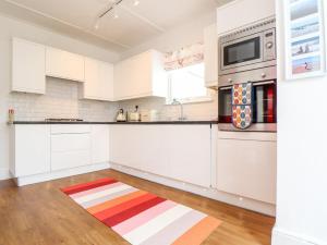 une cuisine avec des placards blancs et un tapis rouge et blanc dans l'établissement Mazey Cottage, à Penzance 22 autres photos