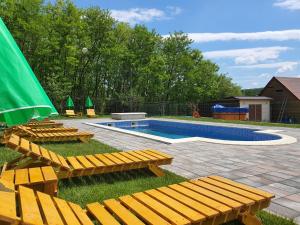 a swimming pool with wooden chairs and a green umbrella at Pensiunea Stan in Cisnădie