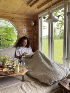 una mujer sentada en un sofá leyendo un libro en Treehouse escape, en Kværndrup
