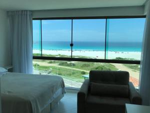 a bedroom with a bed and a chair and a large window at Sophia II Residence Inn in Arraial do Cabo