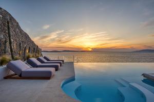 a infinity pool with lounge chairs and a sunset at Villa Santa Esmeralda Mykonos in Agios Ioannis Mykonos
