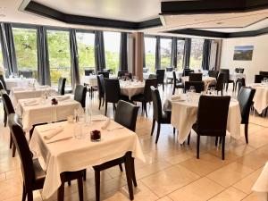 un restaurante con mesas y sillas blancas y ventanas en Hôtel Restaurant Lamy, en Troisvierges