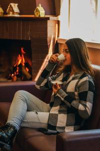 uma mulher sentada num sofá a beber uma chávena de café em Green Village Hotel em Monte Verde