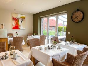 un restaurante con mesas y sillas blancas y un reloj en Hotel Grachtenhuus Greetsiel, en Greetsiel