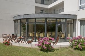 ein Glasgebäude mit einer Terrasse mit Tischen und Stühlen in der Unterkunft Aparthotel Adagio Access Paris Vanves - Porte de Châtillon in Vanves