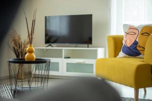 a living room with a yellow chair and a television at TREND BA HOME Apartman in Balatonalmádi