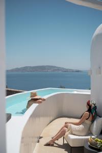 a woman sitting on a chair next to a swimming pool at Rocabella Mykonos Hotel in Agios Stefanos