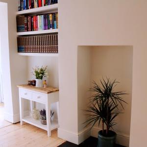 a book shelf with books on it next to a table with a plant at Beautiful Victorian Home near central Oxford in Oxford