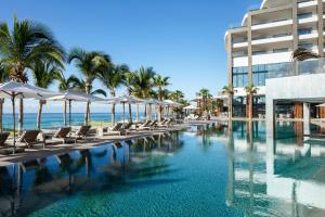 a swimming pool with chairs and umbrellas and the ocean at Garza Blanca Resort & Spa Los Cabos in Cabo San Lucas