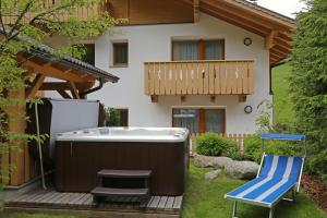 uma banheira de hidromassagem e uma cadeira num deque em frente a uma casa em Almhotel Bergerhof em Sarentino