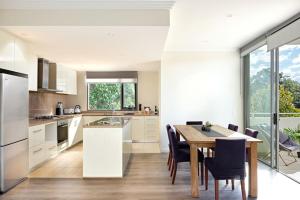 cocina con armarios blancos, mesa y sillas en Large Premium Warrawee Apartment with Parking A401 en Warrawee