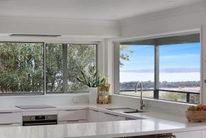eine Küche mit weißen Arbeitsplatten und Fenstern mit Aussicht in der Unterkunft Rosie's Seaview-Lake to ocean view in Merimbula + 48 Fotos