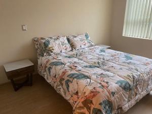 a bedroom with a bed with a floral comforter and a table at Departamento Centro Chillan in Chillán
