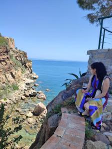 a woman sitting on a path by the water at Kalura Sea House in Cefalù