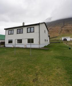 una casa bianca in un campo di fronte a una montagna di Scenic Village / Nature / Cozy House / 4 BR a Viðareiði