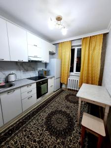 una cocina con armarios blancos y una mesa y cortinas amarillas en 2 комнатная квартира Назавбаева 34, en Pavlodar