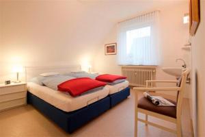 Schlafzimmer mit einem Bett mit roten Kissen und einem Waschbecken in der Unterkunft Ferienhaus Mien Huske in Norderney