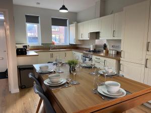 Heartswood Home Modern 3-bedroom, double driveway في Bentley: مطبخ مع طاولة خشبية مع لوحات واكواب للنبيذ
