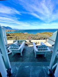 drie witte stoelen op een patio met uitzicht op de oceaan bij 11 WESTCLIFF RENTALS in Hermanus