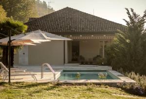 a swimming pool with an umbrella and a house at Parco Reala // Rural - Luxury - Rooms in Corneliano d'Alba