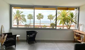 a room with a large window with palm trees and the ocean at Plage Landsberg Appartement 2 pièces en bord de mer in Saint-Laurent-du-Var