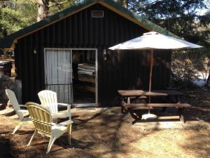 - une table de pique-nique, des chaises et un parasol en face d'une cabine dans l'établissement Amber Lantern Two-Bedroom Cottage, à Lake George 1 autre photo