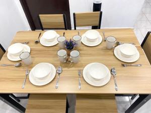 a wooden table with white plates and silverware on it at Cozy Murni 14th Entire 3 Bedroom House at Alma Bkt Mertajam in Bukit Mertajam +29 photos