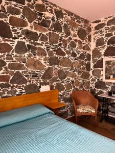 a bedroom with a stone wall with a bed and a chair at Casa rural con baño adaptado y piscina en Mogán in Mogán