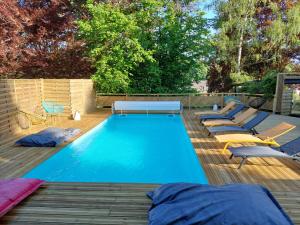 a swimming pool with chaises and chairs on a wooden deck at Le Clos des Lodges in Bernay