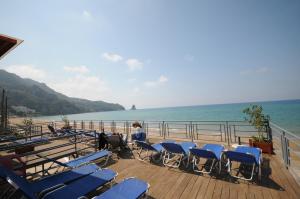 a woman sitting on a deck with chairs and the ocean at Pink Palace Beach Resort in Agios Gordios