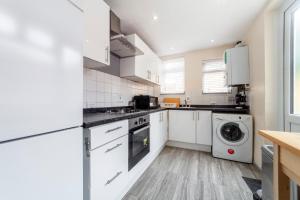 a kitchen with white cabinets and a washer and dryer at Highlands Gardens Suites in Ilford