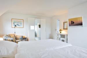 a white bedroom with a bed and a chair at Westcoast in Hörnum